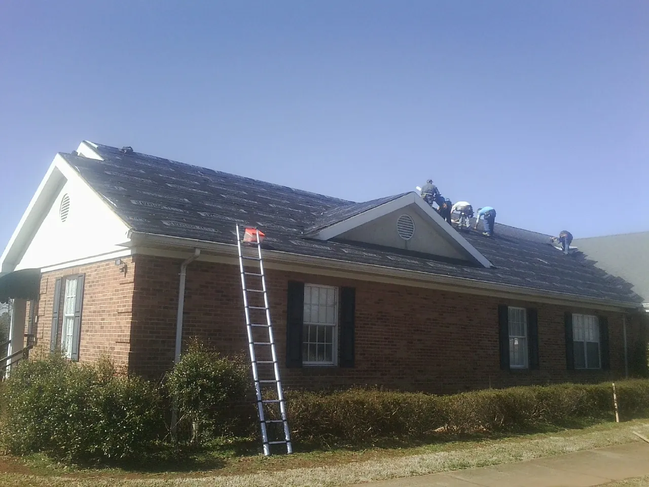 Crew tearing shingles off a brick ranch roof with a ladder set — Emergency Roof Repair work by our crew in Santa Fe Springs