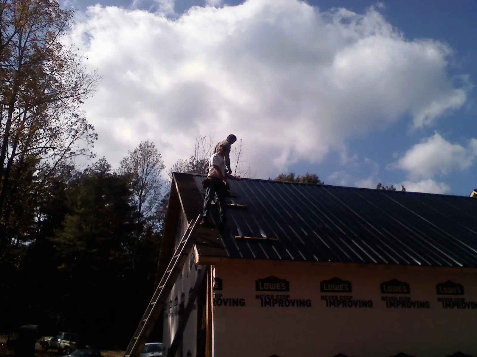 Roofer fastening dark metal panels high against a cloudy sky, from a Roof Inspection job in Santa Fe Springs