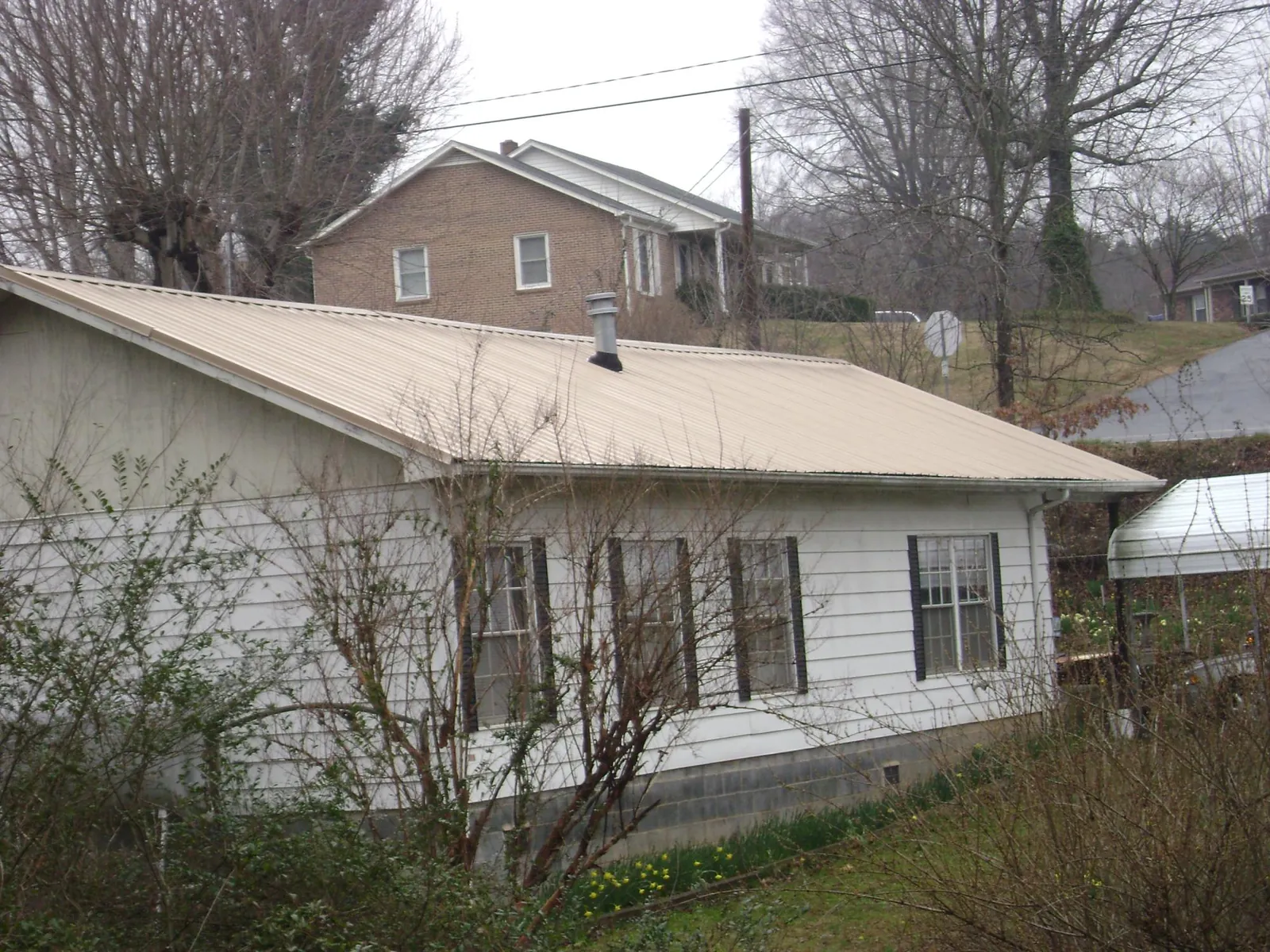 Tan metal roof on a white sided house set into a hillside — Commercial Roofing by Roofing Brothers in Santa Fe Springs