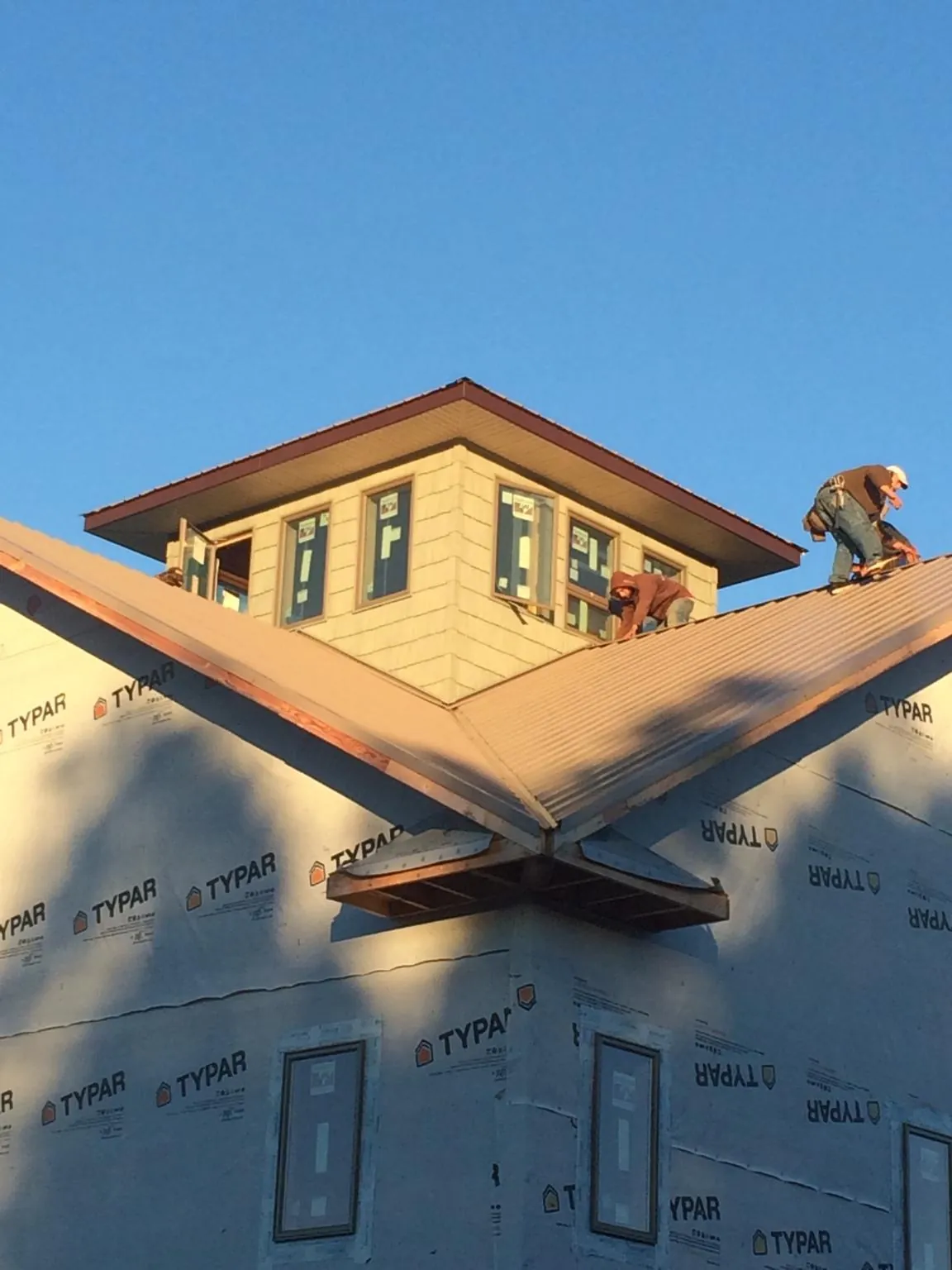 Roofers working around a rooftop cupola on a new metal roof at sunset — Roof Waterproofing in Santa Fe Springs by Roofing Brothers